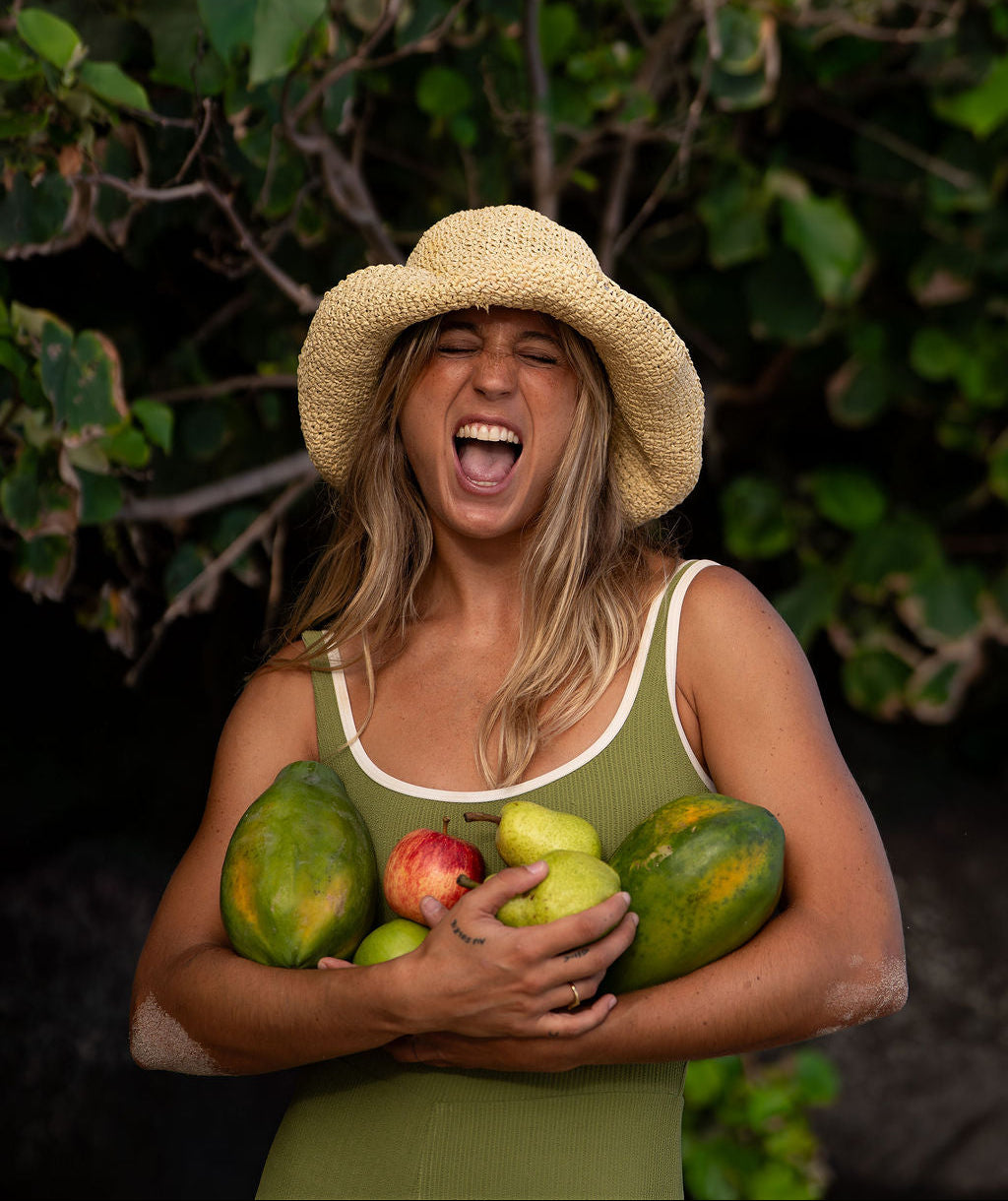 Woman holding fruits and vegetables outdoors with a green leafy background